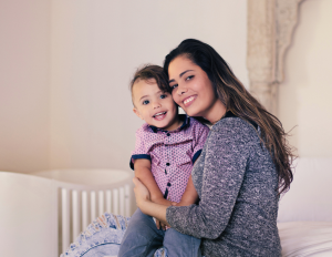 Mother holding her young child and smiling together in a warm, supportive family setting.